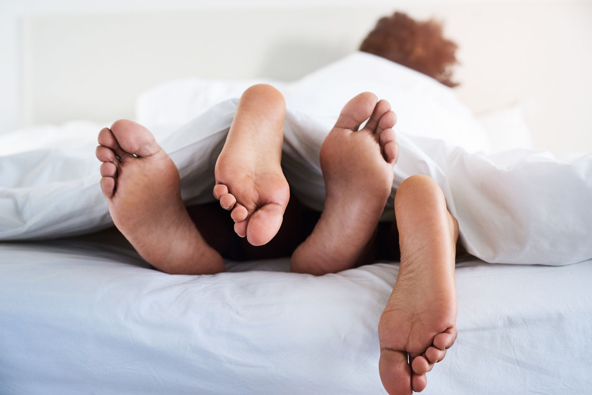 Paar liegt im Bett, Füße schauen unter der Decke hervor