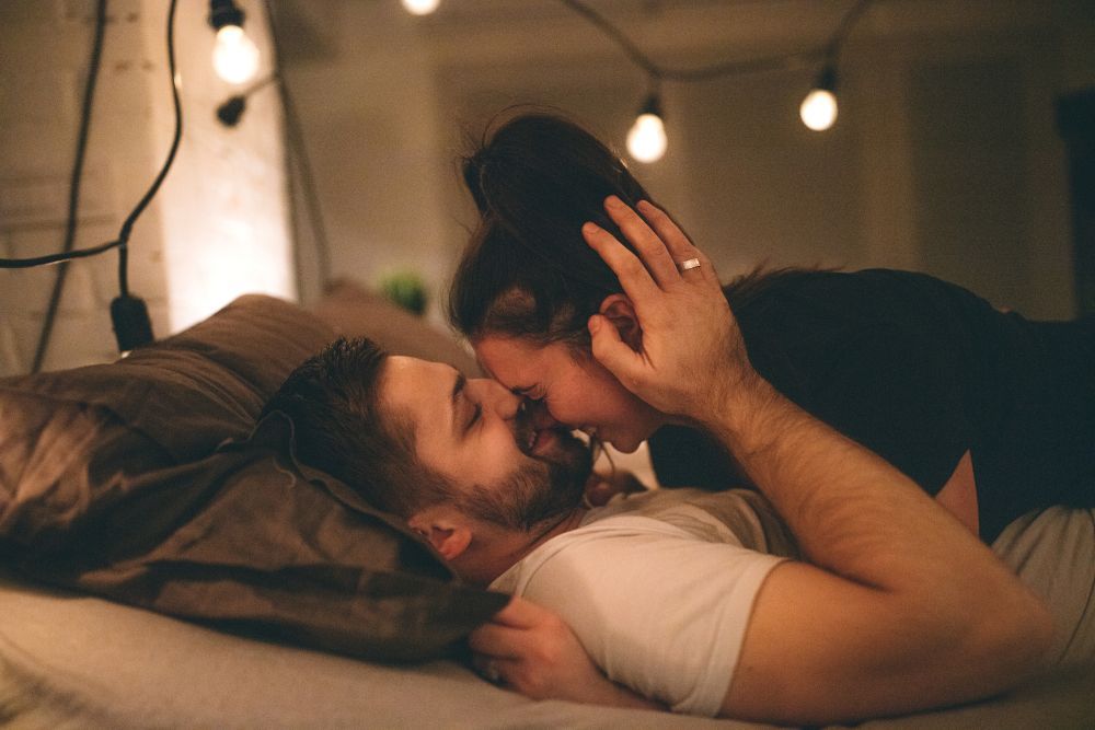 Ein Pärchen liegt bekleidet im Bett, er küsst sanft ihre Nase