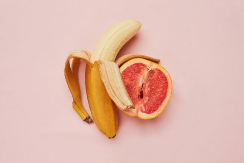 Eine Banane und eine Blut-Orange die nebeneinander liegen vor einem rosanen Hintergrund