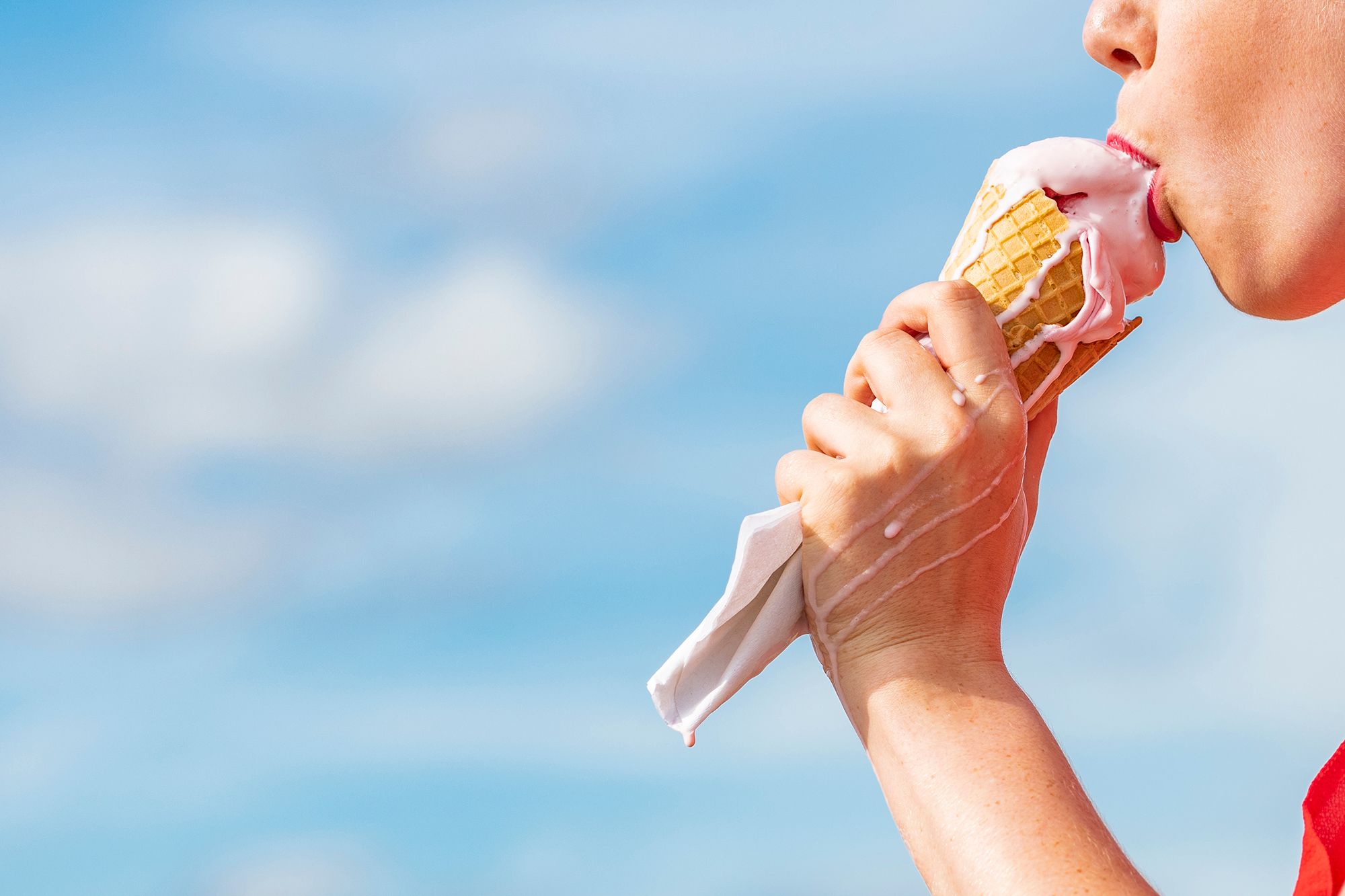 Frau leckt an zerlaufenem Eis vor blauem Himmel