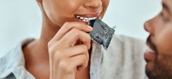 Frau öffnet eine Kondompackung mit den Zähnen