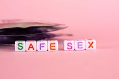 Kondompackungen, vor denen die Buchstaben Safe Sex auf würfen stehen
