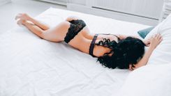 Frau in schwarzen Dessous liegt bäuchlings auf dem Bett