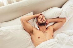 Mann liegt im Bett und genießt einen Blowjob