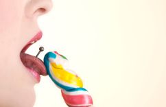 Frau mit Zungenpiercing leckt an einem Lolli