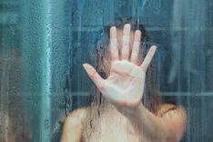 Selbstbefriedigung in der Dusche - Abbildung einer nackten Frau, welche ihre Hand von innen gegen die Glas-Duschkabine drückt, ihre Handfläche im Fokus, ihr Körper in der Unschärfe.