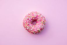 Donut mit rosa Glasur und bunten Streuseln auf rosa Hintergrund