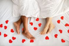 Paar im Bett mit roten Papierherzen auf dem Laken