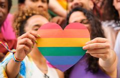 Zwei Frauen halten ein Herz mit Regenbogen Streifen hoch