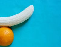 Banane und halbe Orange vor blauem Hintergrund, die einen Penis und Hoden formen