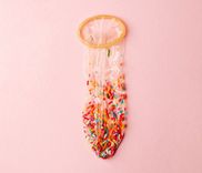 Mit Schokostreuseln gefülltes Kondom vor rosa Hintergrund