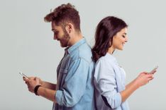 Mann und Frau stehen Rücken an Rücken und haben Handys in der Hand