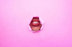 Mund, der ein Kaugummi leicht aufbläst hinter einer pinkfarbenen Papierwand mit einem Loch