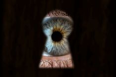 Eine Person mit blauen Augen späht durch ein Schlüsselloch.