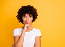 Frau in weißem T-Shirt vor orangenem Hintergrund guckt nachdenklich zur Seite