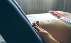 Nahaufnahme vom Bauch einer schwangeren Frau in gestreiftem T-Shit und blauer Leggings auf einem Bett