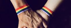 Zwei verschränkte Hände mit Regenbogen-Armbändern