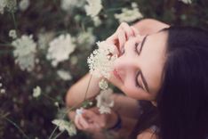 Frau sitzt in einer Wiese und riecht an einer Blume