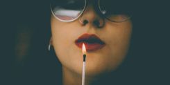 Eine Frau mit Nasenpiercing hält ein angezündetes Streichholz vor den Lippen