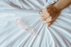Hand krallt sich an der Bettdecke fest, daneben liegt ein benutztes Kondom