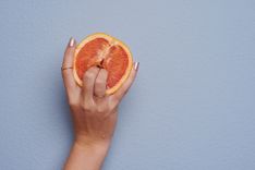 Frauenhand die mit zwei Fingern in eine Grapefruit sticht