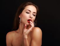 Leichtbekleidete Frau mit roten Lippen, die lasziv mit geschlossenen Augen in die Kamera schaut vor schwarzem Hintergrund