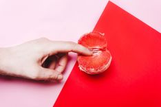 Finger in einer Grapefruit auf rot-rosa Hintergrund