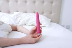 Frau liegt im Bett und hält einen Vibrator in der Hand