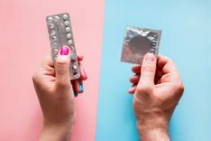 Pillen-Blister vor rosa Hintergrund und verpacktes Kondom vor blauem Hintergrund, die beide jeweils von einer Hand gehalten werden