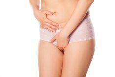 Frau in Slip, die sich eine Hand auf den Bauch und die andere vor den Intimbereich hält auf weißem Hintergrund
