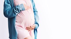 Schwangere Frau in rosa Kleidchen und blauem Cardigan vor weißem Hintergrund