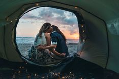 Zwei Personen sitzen vor einem Zelt am Strand und küssen sich.