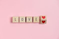 Holzbuchstaben mit der Aufschrift "Love" und einem roten Herz auf rosa Hintergrund