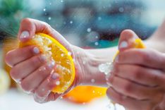 Frau mit weißen Fingernägeln, die jeweils eine halbe Orange in ihren Händen zerdrückt
