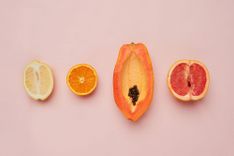 Halbierte Zitrone, Orange, Papaya und Grapefruit, die nebeneinander liegen, auf beigem Hintergrund