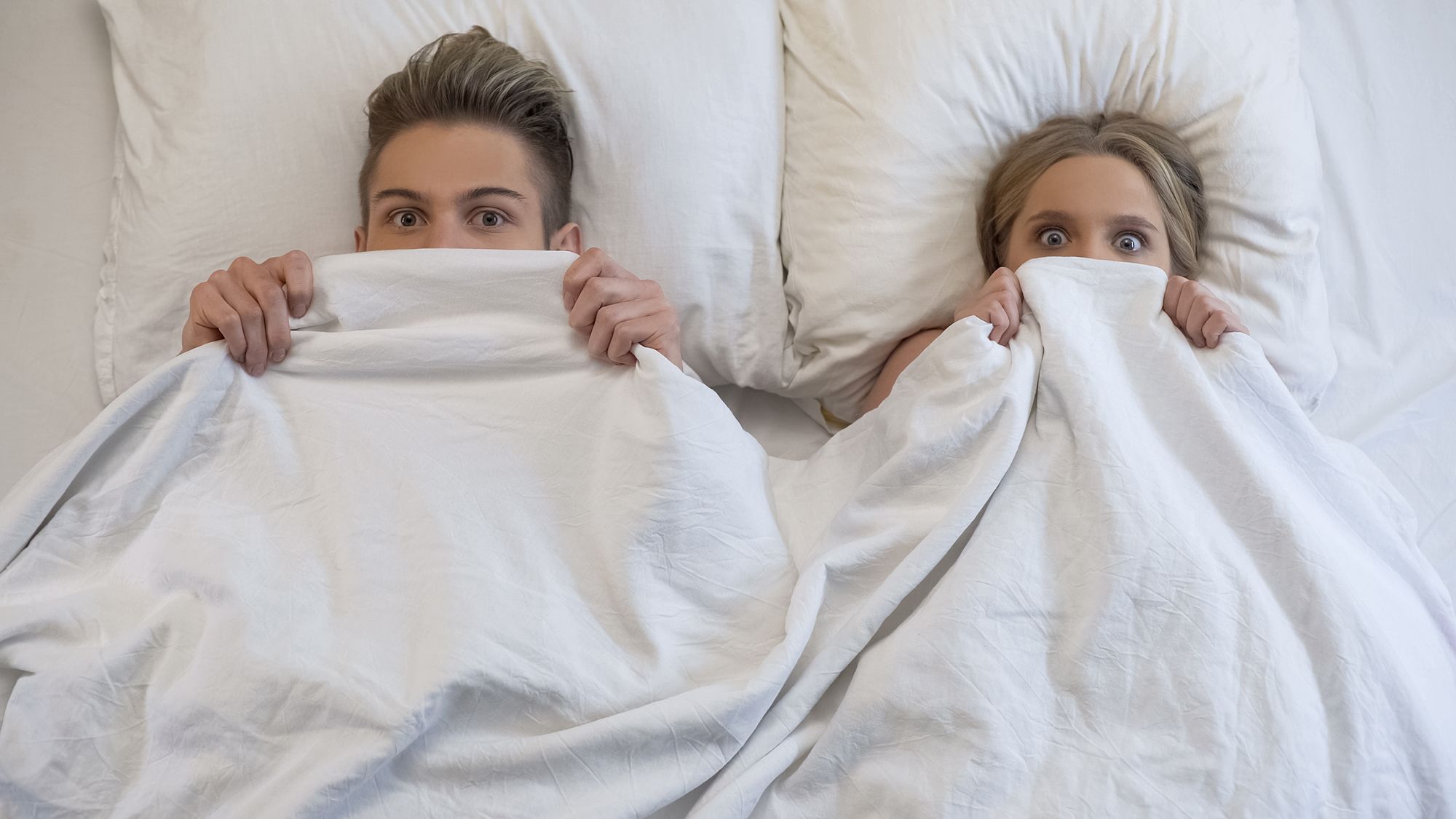 Mann und Frau im Bett haben die Decke bis zu den Augen hochgezogen