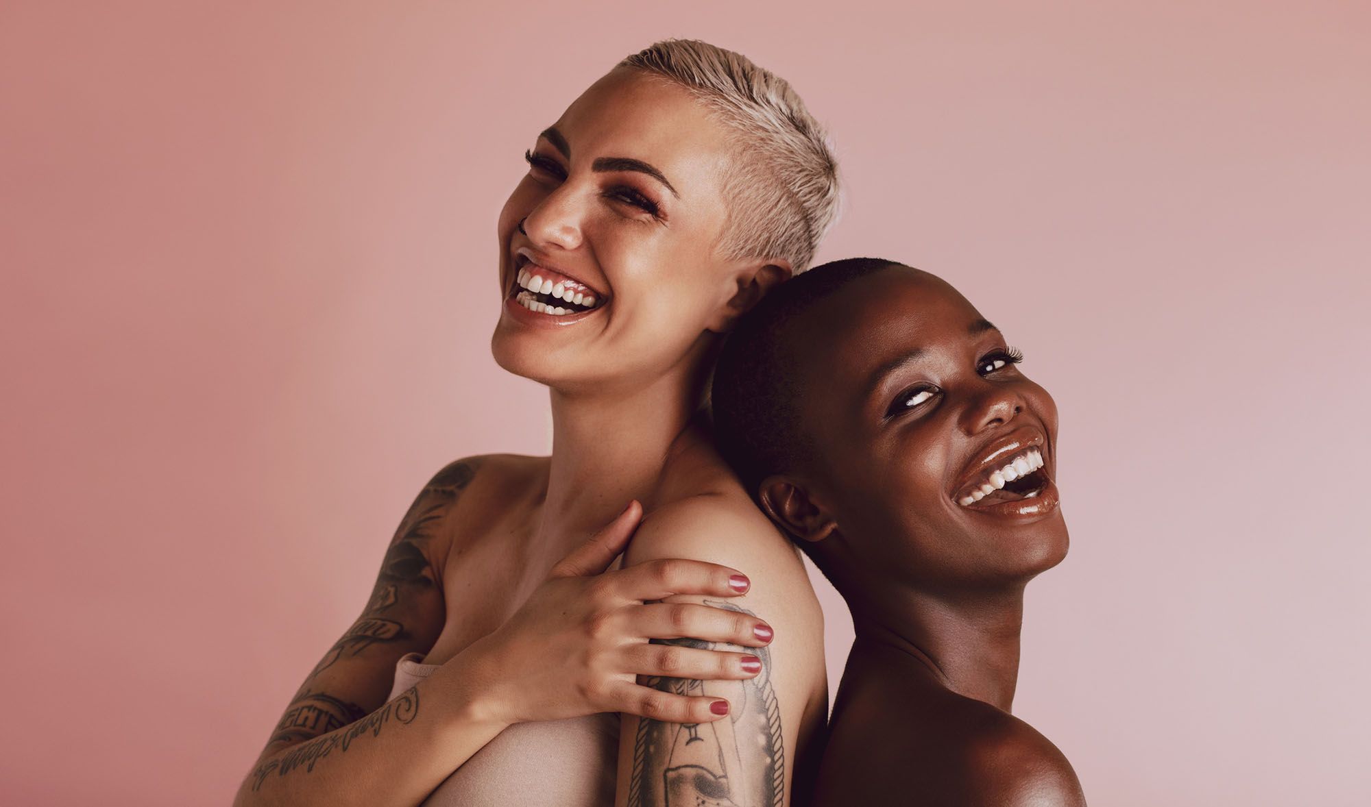 Welt-Orgasmus-Tag: Zwei Frauen, die Rücken an Rücken stehen und glücklich lachen