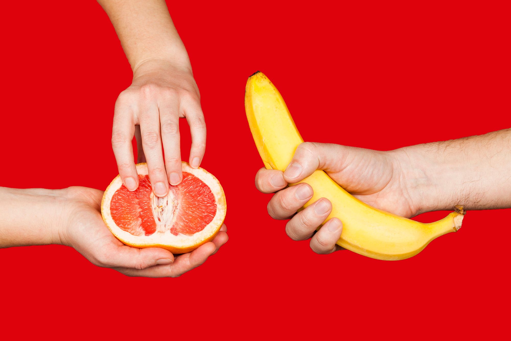 Eine Hand, die eine Banane hält und zwei weitere Hände, die eine halbierte Grapefruit halten vor rotem Hintergrund